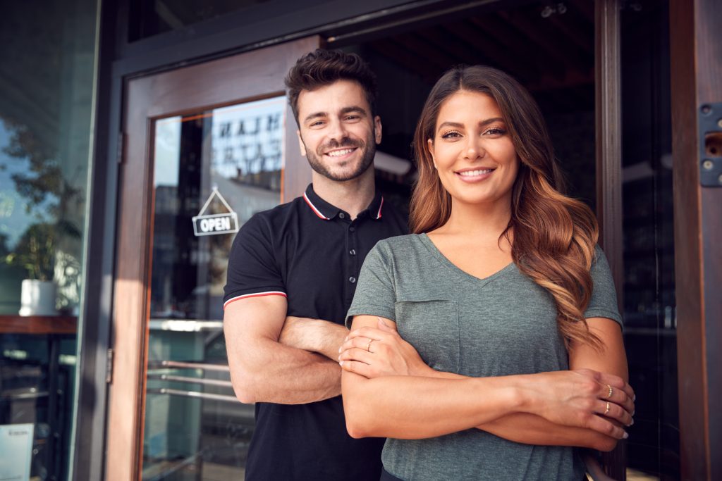 Portrait of couple starting an LLC standing in front of their business location.